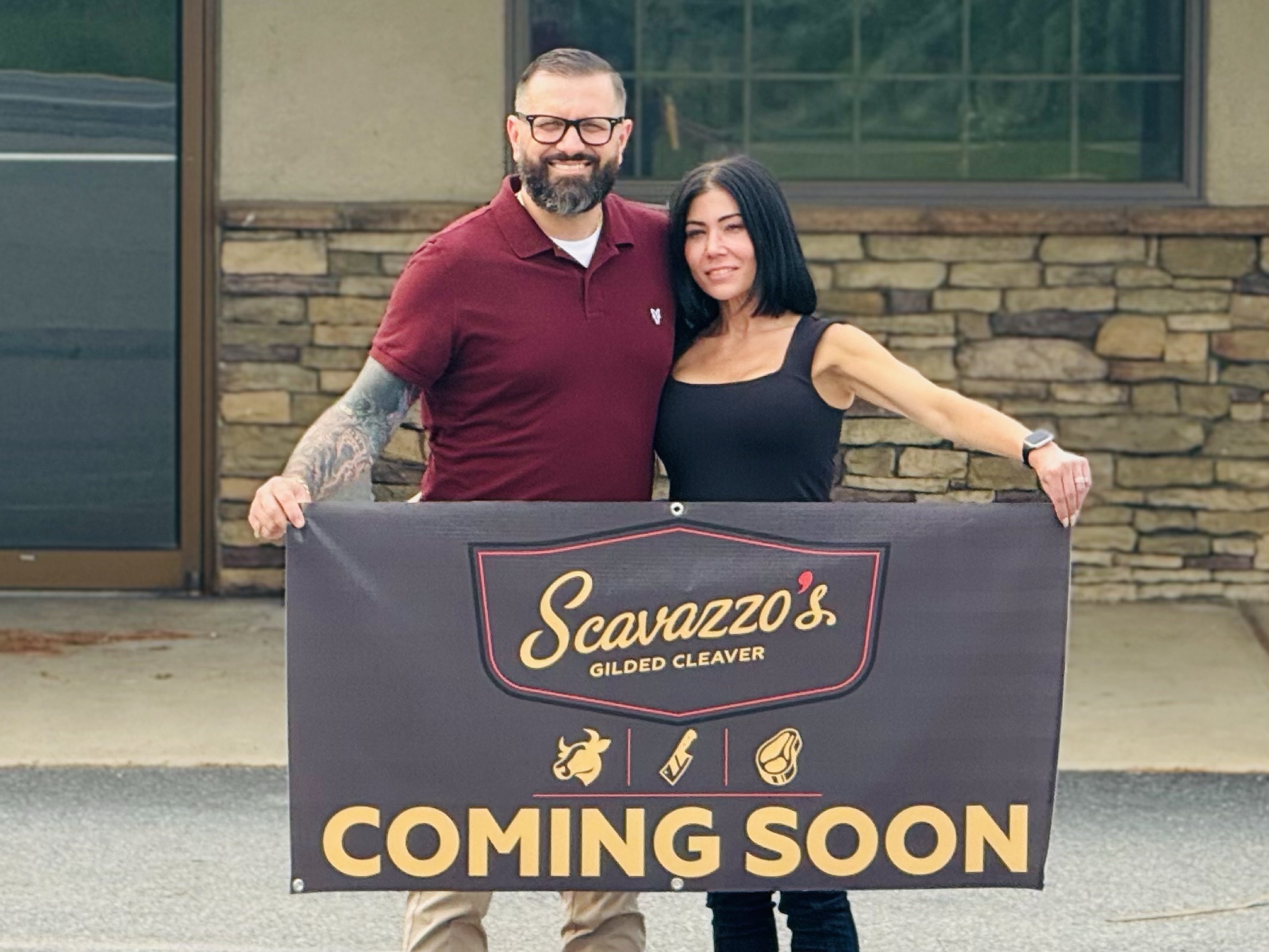 Jeremy and Allison Scavazzo outside Nor-Bath Plaza with the Scavazzo's Gilded Cleaver Coming Soon banner